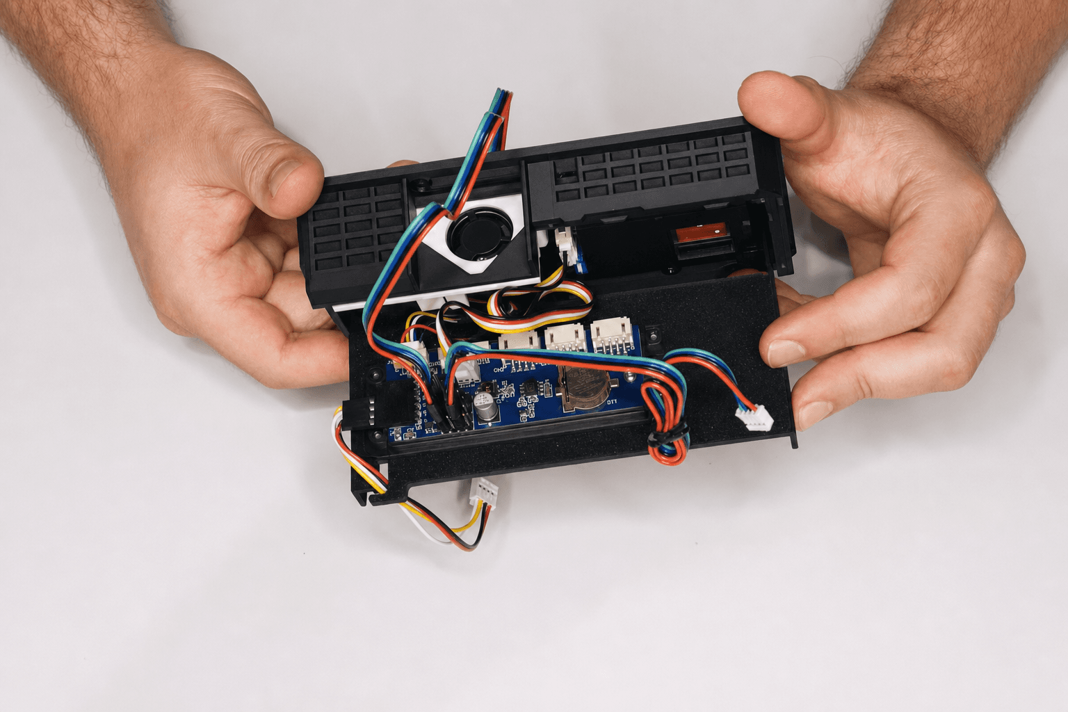 Opened Aura AQ enclosure held in both hands with the PCB, connectors and cable routing visible